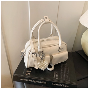 Detail der cremefarbenen Boston Bag mit Vordertaschen und Perlen-Herzanhänger