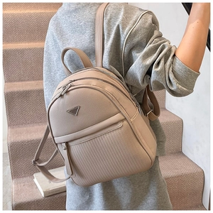 Detail of beige pebble leather backpack with triple zippers and triangle metal plaque