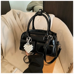 Detail der schwarzen Lackleder Boston Tasche mit Perlenherz-Anhänger auf dem Sofa