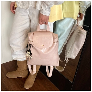 Close-up of beige glossy PU leather backpack with a striped doll charm and top handle