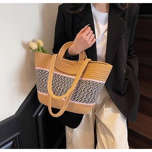 Detail of hand-woven straw tote bag with black and white checkered strap and floral accent