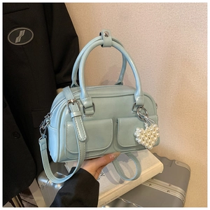 Close-up of light blue glossy Boston bag with front pockets and pearl heart pendant