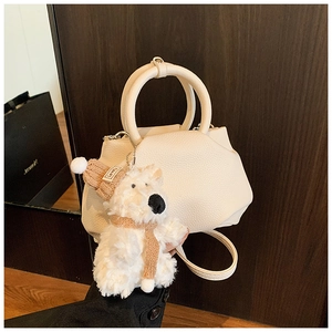 Detail of cream lychee leather bucket bag with a cute plush puppy charm and round handle