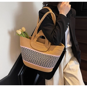 Detail of a large khaki woven tote bag with pink trim and decorative black-and-white ribbon