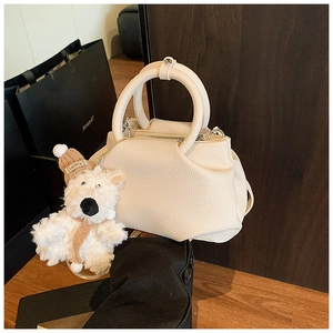 Detail of cream pleated leather bucket bag with plush bear charm on wooden surface