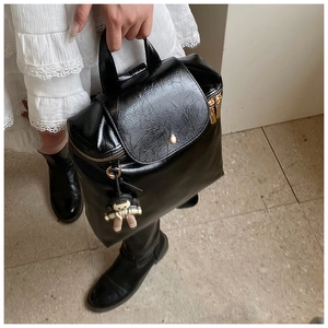 Detail of black glossy crinkle leather backpack with gold hardware and charm