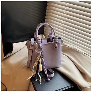 Detail of lavender bucket bag with knot handle and charm on top of a hardcover book