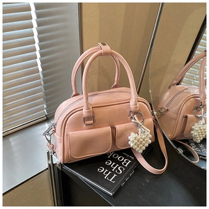 Detail der rosa Boston Bag mit zwei Griffen und einem Perlen-Herzanhänger auf einer Spiegelfläche