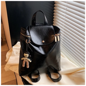 Detailed view of black pleated glossy backpack featuring gold hardware and a cute doll charm