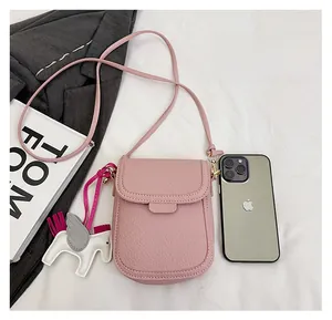 Détail macro du sac à téléphone en cuir rose grainé avec breloque cheval décorative