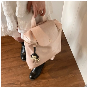 Detail of light pink textured leather backpack with metal buckle and cute doll pendant
