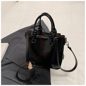 Detail of glossy black bucket bag featuring knotted handles and metal zipper closure