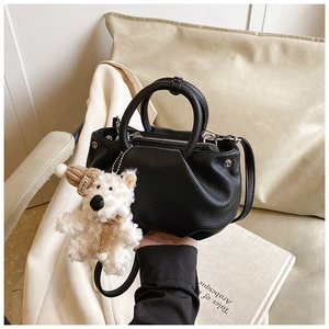 Close-up of black lychee grain leather bucket bag with a cute teddy bear charm