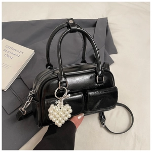 Detail einer glänzenden schwarzen Boston-Bag mit Vordertaschen und Herz-Perlenanhänger