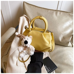 Detail of yellow lychee grain leather handbag featuring a cute plush bear charm accessory