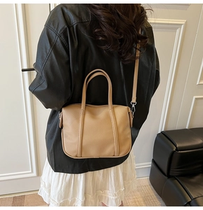 Rear view of a beige pebble leather handbag worn over the shoulder by a model