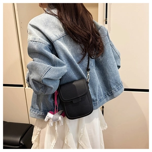 Détail d'un sac à bandoulière en cuir grainé noir avec un charm de cheval blanc porté