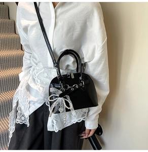 Sac bandoulière noir chic avec nœud en dentelle et chaîne perlée sur chemise blanche