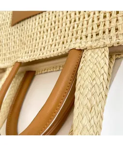 Detail of woven straw bag showing the texture, leather handle and adjustable shoulder strap