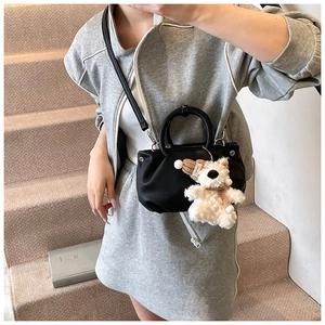 Close-up of black lychee grain pleated bucket bag with cute plush animal charm on a model