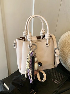 Minimalist beige bucket bag with decorative pendants and adjustable crossbody strap