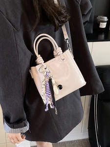 Chic beige bucket bag with knot handle and decorative charms on a stylish blazer