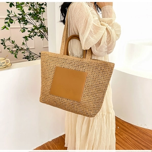 Large straw tote bag with brown leather patch and dual handles shown in a lifestyle setting