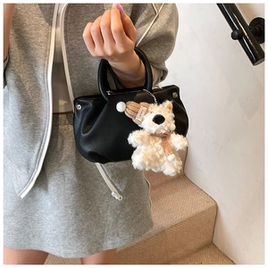 Detail of black litchi grain leather handbag featuring a cute plush bear charm with hat