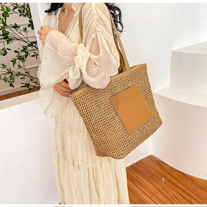 Detail of a large woven straw tote bag with brown leather patch and long shoulder straps