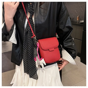 Détail d'un petit sac bandoulière rouge avec motif litchi et charm licorne en cuir
