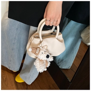 Detail of cream lychee leather handbag with a cute plush puppy charm wearing a brown hat