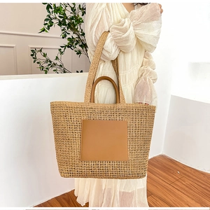 Detail of a large straw tote bag with brown leather patch and handles for summer