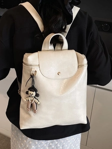 Minimalist off-white faux leather backpack with metallic buckle and cartoon charm accessory