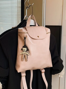 Fashionable light pink backpack with cartoon charm hanging on a black jacket