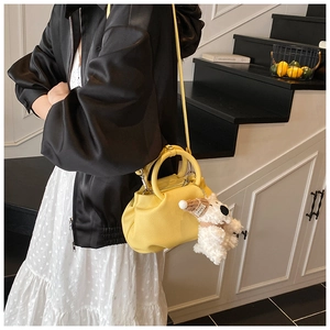 Detailed shot of yellow pleated bucket bag with cute plush puppy charm and round handle