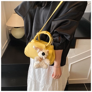 Detail of yellow pleated bucket bag with plush bear charm and crossbody strap