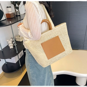 Detail of woven straw tote bag featuring brown leather patch and rounded top handles