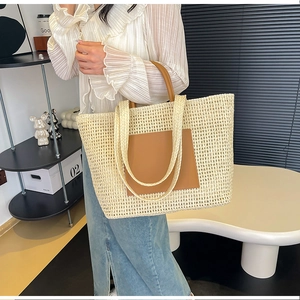 Detail of a large beige woven tote bag featuring a leather pocket and shoulder straps