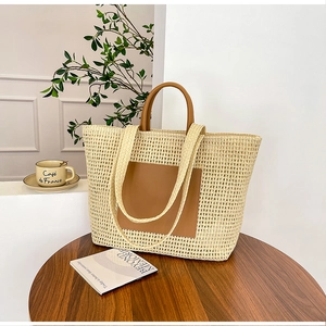 Close-up of a woven straw tote bag with brown leather handles and a front pocket