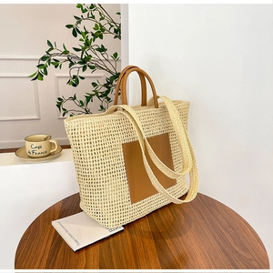 Detail of woven straw tote bag featuring brown leather patch and dual handles on a table