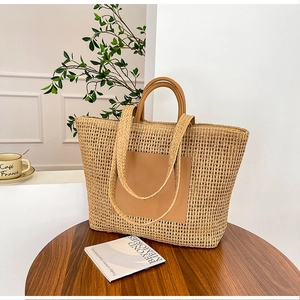 Detail shot of large woven straw tote bag with brown leather handles on wooden table