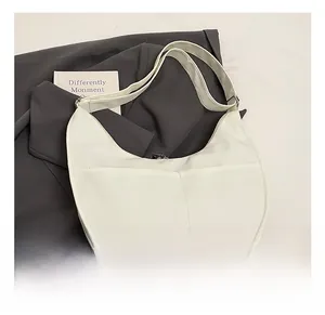 Detail shot of the white moon-shaped crossbody bag on a grey blazer showing smooth PU leather