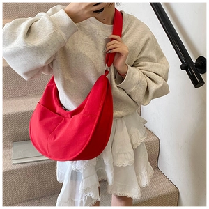 Detail of red canvas crescent bag with adjustable wide strap shown on a casual outfit