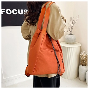 Detail view of large orange nylon tote bag with drawstring on a modern studio background