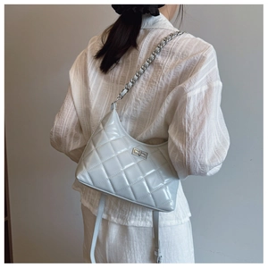 Détail du sac matelassé brillant avec bandoulière chaîne sur une chemise à rayures blanches