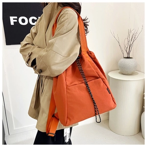 Side view of large orange drawstring bucket bag worn by model in casual trench coat