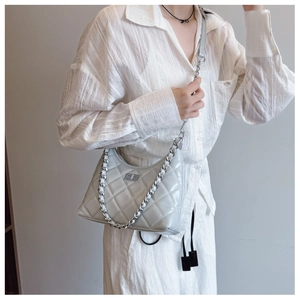 Sac bandoulière gris matelassé avec chaîne argentée porté sur une tenue blanche