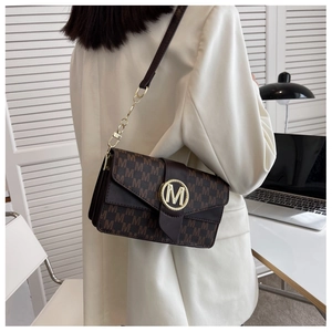 Sac à main marron à monogramme avec boucle M dorée porté sur un blazer blanc chic