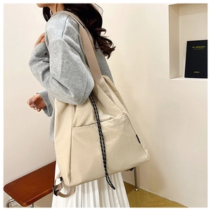 Side view of large off-white nylon tote bag with wide strap and decorative drawstrings