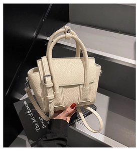 Detail of cream white leather handbag featuring dual handles and detachable shoulder strap